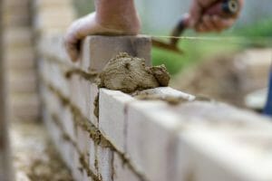 The experienced hands of a bricklayer as he lays the next course of bricks