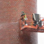 man in a lift pressure washing a brick tower